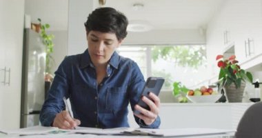 Beyaz kadın evde akıllı telefon kullanarak notlar alıyor ve mali hesaplar yapıyor. Aile finansmanı ve bütçe kavramı