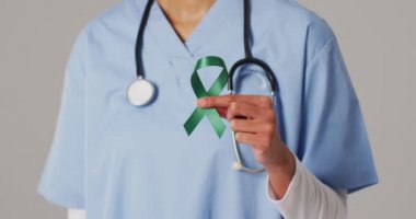 Zümrüt karaciğer kanseri kurdelesi tutan gülümseyen melez kadın doktorun videosu. küresel tıp ve sağlık konsepti.