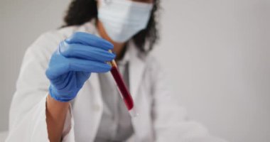 Test tüpü tutan ve mavi arka planda dizüstü bilgisayar kullanan melez bir kadın doktorun videosu. küresel tıp ve sağlık konsepti.