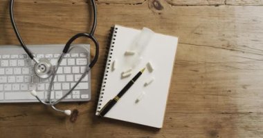 Steteskopun yakın çekim videosu, defter ve haplar ahşap masanın üzerinde. küresel tıp ve sağlık konsepti.