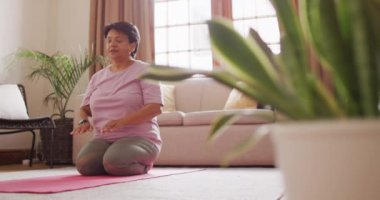 Üst düzey melez kadın oturma odasında yoga ve meditasyon yapıyor. evde sağlıklı ve aktif emeklilik.