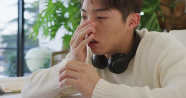 Kulaklıklı Asyalı genç erkek oturma odasında laptop öğreniyor ve kullanıyor. Evde yalnız zaman geçirmek..