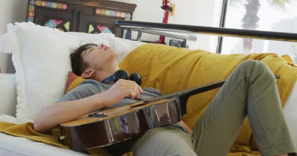 Asiático Adolescente Masculino Con Auriculares Tocando Guitarra Acostado Sala Estar — Vídeos de Stock