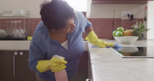 手袋を着用し キッチンだけで掃除台を身に着けている高齢の出産の女性を笑顔 家での健康的で活発な退職は — ストック動画