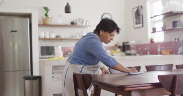 Senior Biracial Woman Wearing Apron Cleaning Table Kitchen Alone Healthy — Αρχείο Βίντεο