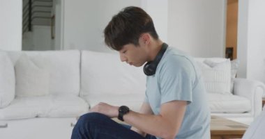 Oturma odasında kulaklık takan mutlu Asyalı bir gencin portresi. Evde yalnız zaman geçirmek..