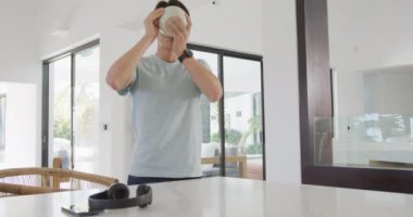 Asyalı genç erkek, kulaklıklarını akıllı telefonuyla kapıp kahvaltı yapıyor. Evde yalnız zaman geçirmek..