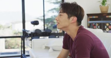 Mutlu Asyalı genç erkek televizyon izliyor ve oturma odasında oturuyor. Evde yalnız zaman geçirmek..