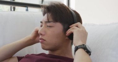 Asyalı genç erkek oturma odasında kulaklıkla müzik dinliyor. Evde yalnız zaman geçirmek..