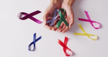 Video of hands of caucasian woman holding colorful ribbons on white background. medicine, health, cancer awareness concept digitally generated video.