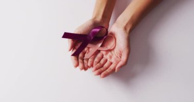 Beyaz arka planda menekşe ve pembe kurdeleler tutan beyaz bir kadının elleri. tıp, sağlık, kanser farkındalığı konsepti dijital olarak üretilen video.