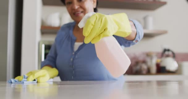 Smiling Senior Biracial Woman Wearing Gloves Cleaning Table Kitchen Alone — Wideo stockowe