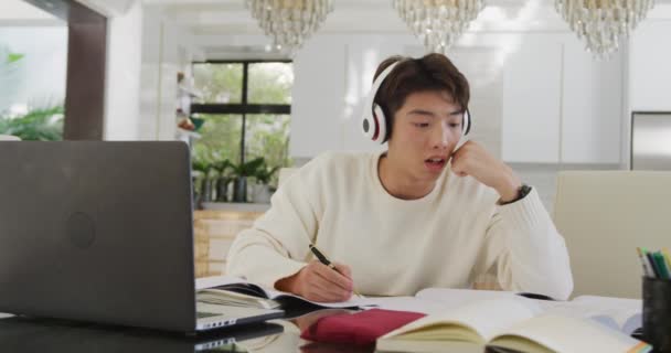 ヘッドフォン学習とリビングルームでラップトップを使用してアジアの男性ティーンエイジャー 家で一人で過ごす — ストック動画
