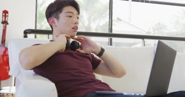 Asian Male Teenager Wearing Headphones Using Laptop Living Room Spending — Video