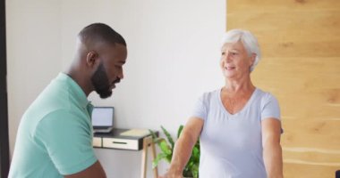Video of happy african american male physiotherapist examining caucasian senior woman. seniors health and nursing home lifestyle concept.