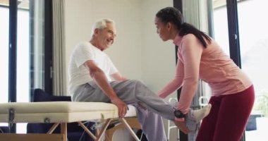 Kafkasyalı kıdemli adamı inceleyen melez kadın fizyoterapistin videosu. Yaşlılar sağlığı ve huzurevi konsepti dijital olarak oluşturulmuş video.