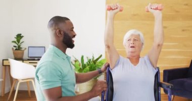 Video of happy african american male physiotherapist exercising with caucasian senior woman. seniors health and nursing home lifestyle concept.