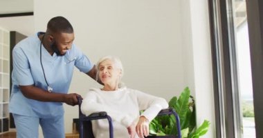 Video of happy african american male doctor taking care of caucasian senior woman. seniors health and nursing home lifestyle concept.