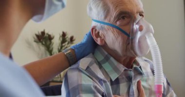 Beyaz yaşlı bir adama oksijen veren maskeli melez kadın doktorların videosu. Yaşlılar sağlık ve huzurevi konsepti.