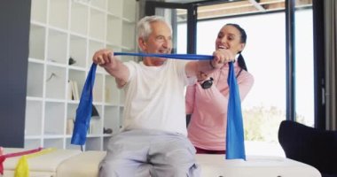Video of happy biracial female physiotherapist exercising with caucasian senior man. seniors health and nursing home lifestyle concept digitally generated video.