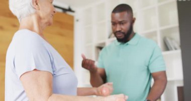 Afrika kökenli Amerikalı erkek fizyoterapistin beyaz yaşlı kadınla egzersiz yaptığı bir video. Yaşlılar sağlık ve huzurevi konsepti.