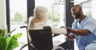 Kafkasyalı yaşlı kadınla ilgilenen mutlu Afrikalı Amerikalı erkek doktorun videosu. Yaşlılar sağlık ve huzurevi konsepti.