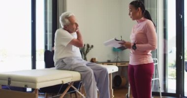 Kafkasyalı kıdemli adamı inceleyen melez kadın fizyoterapistin videosu. Yaşlılar sağlığı ve huzurevi konsepti dijital olarak oluşturulmuş video.