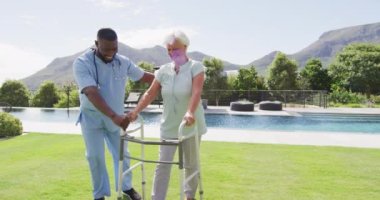 Bahçedeki beyaz yaşlı kadınla ilgilenen mutlu Afrikalı Amerikalı erkek doktorun videosu. Yaşlılar sağlık ve huzurevi konsepti.