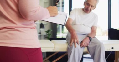 Beyaz adamı inceleyen melez kadın fizyoterapistin orta bölüm videosu. Yaşlılar sağlığı ve huzurevi konsepti dijital olarak oluşturulmuş video.