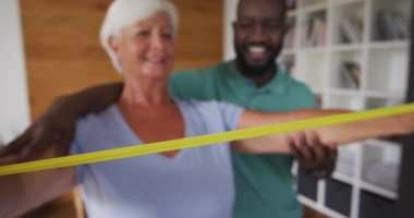 Afrika kökenli Amerikalı erkek fizyoterapistle egzersiz yapan mutlu, beyaz bir kadının videosu. Yaşlılar sağlığı ve huzurevi konsepti dijital olarak oluşturulmuş video.