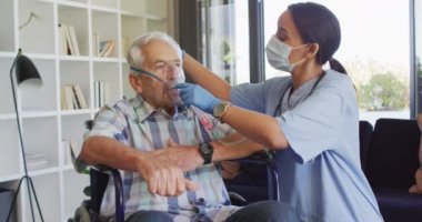 Video of biracial female doctor in face mask keeping oxygen to caucasian senior man. seniors health and nursing home lifestyle concept.