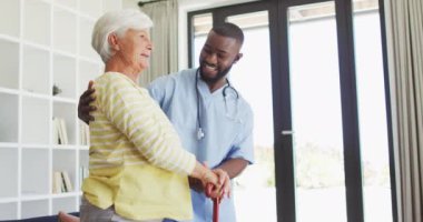 Kafkasyalı yaşlı kadını destekleyen mutlu Afrikalı Amerikalı erkek doktorun videosu. Yaşlılar sağlık ve huzurevi konsepti.
