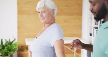 Afrika asıllı Amerikalı erkek fizyoterapistin beyaz yaşlı kadınla egzersiz yaptığı bir video. Yaşlılar sağlık ve huzurevi konsepti.