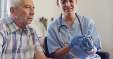 Çift ırklı mutlu kadın doktorun beyaz yaşlı adamla glikoz seviyesini kontrol ettiği bir video. Yaşlılar sağlık ve huzurevi konsepti.