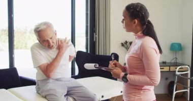 Kafkasyalı kıdemli adamı inceleyen melez kadın fizyoterapistin videosu. Yaşlılar sağlığı ve huzurevi konsepti dijital olarak oluşturulmuş video.