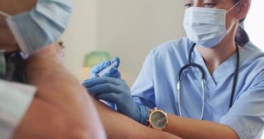 Video of hands of biracial female doctor vaccinating caucasian senior man. seniors health and nursing home lifestyle concept.