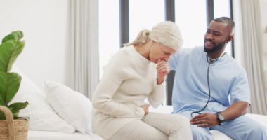 Kafkasyalı yaşlı kadınla ilgilenen mutlu Afrikalı Amerikalı erkek doktorun videosu. Yaşlılar sağlık ve huzurevi konsepti.