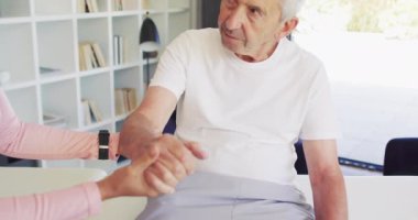 Kafkasyalı kıdemli adamı inceleyen melez kadın fizyoterapistin videosu. Yaşlılar sağlığı ve huzurevi konsepti dijital olarak oluşturulmuş video.