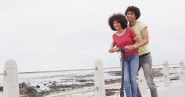 Sahilin yakınındaki gezinti alanında scooter sürerken gülümseyen Afrikalı Amerikalı çift. Aşk ve ilişki kavramı