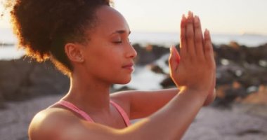 Afrika kökenli Amerikalı kadının yoga yapmasını ve deniz kenarındaki kayalıklarda meditasyon yapmasını yakından izleyin. sağlıklı yaşam tarzı kavramı
