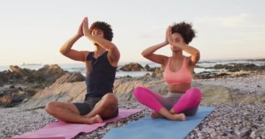 Afrika kökenli Amerikalı çift yoga yapıyor ve deniz kenarındaki kayalıklarda meditasyon yapıyorlar. Aşk ve ilişki kavramı