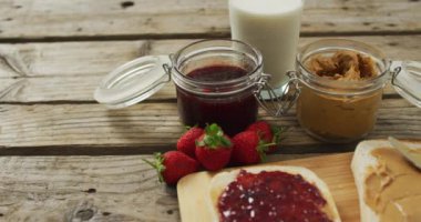 Peanut butter and jelly sandwiches on wooden tray with milk and strawberries on wooden surface. food and nutrition concept