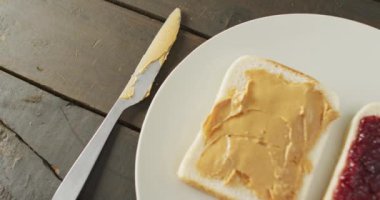 Close up view of peanut butter and jelly sandwiches in a plate with butter knife on wooden surface. food and nutrition concept