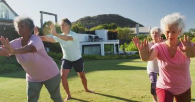 Senior diverse people exercising in garden on sunny day at retirement home. healthy, active retirement and body inclusivity.