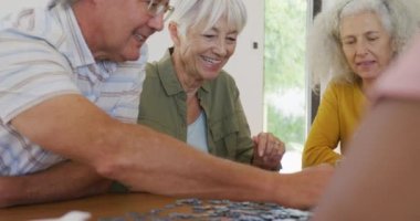 Happy senior diverse people playing puzzle at table at retirement home. healthy, active retirement and body inclusivity.