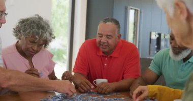 Happy senior diverse people playing puzzle at table at retirement home. healthy, active retirement and body inclusivity.