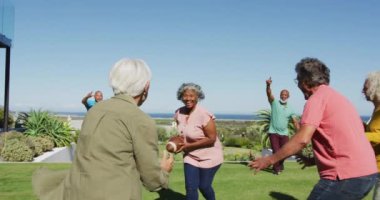 Happy senior diverse people playing rugby in garden at retirement home. healthy, active retirement and body inclusivity.