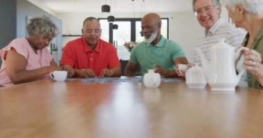 Happy senior diverse people playing puzzle at table at retirement home. healthy, active retirement and body inclusivity.