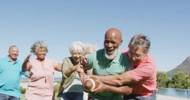 Happy senior diverse people playing rugby in garden at retirement home. healthy, active retirement and body inclusivity.