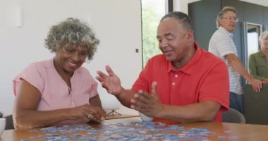 Happy senior diverse people playing puzzle at table at retirement home. healthy, active retirement and body inclusivity.
